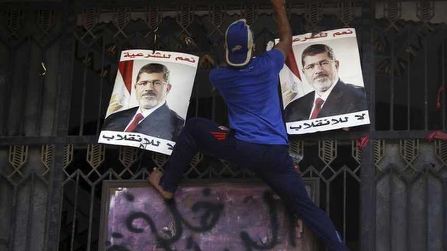 A member of the Muslim Brotherhood and supporter of deposed Egyptian President Mohamed Mursi climbs up the main door of the Attorney General's office to spray a graffiti, which reads "Interior thugs", above posters of Mursi during a protest at the courthouse in downtown Cairo August 5, 2013. Several thousand Islamist supporters of Mursi marched through downtown Cairo on Monday calling for his reinstatement and denouncing the army general who led his overthrow. REUTERS/Amr Abdallah Dalsh (EGYPT - Tags: POLIT