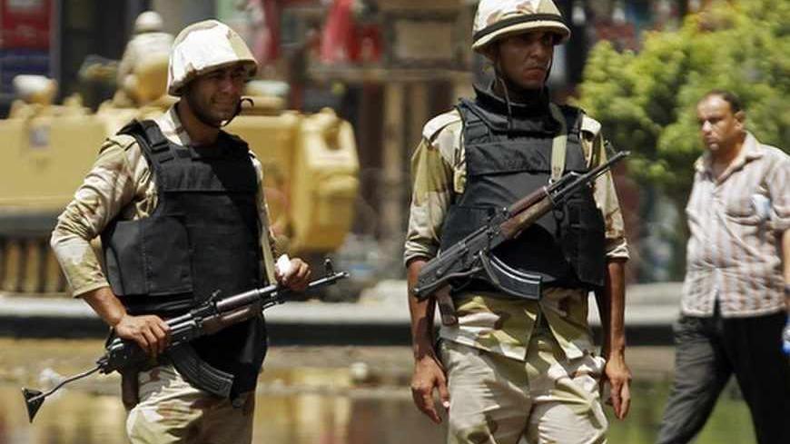 A man walks past behind soldiers in front of an armoured personnel carrier (APC) near the al-Fath mosque on Ramses Square in Cairo August 17, 2013. Egypt's prime minister has proposed disbanding the Muslim Brotherhood of ousted President Mohamed Mursi, the government said on Saturday, raising the stakes in a bloody struggle between the state and Islamists for control of the country. REUTERS/Amr Abdallah Dalsh  (EGYPT - Tags: POLITICS CIVIL UNREST MILITARY) - RTX12OKR