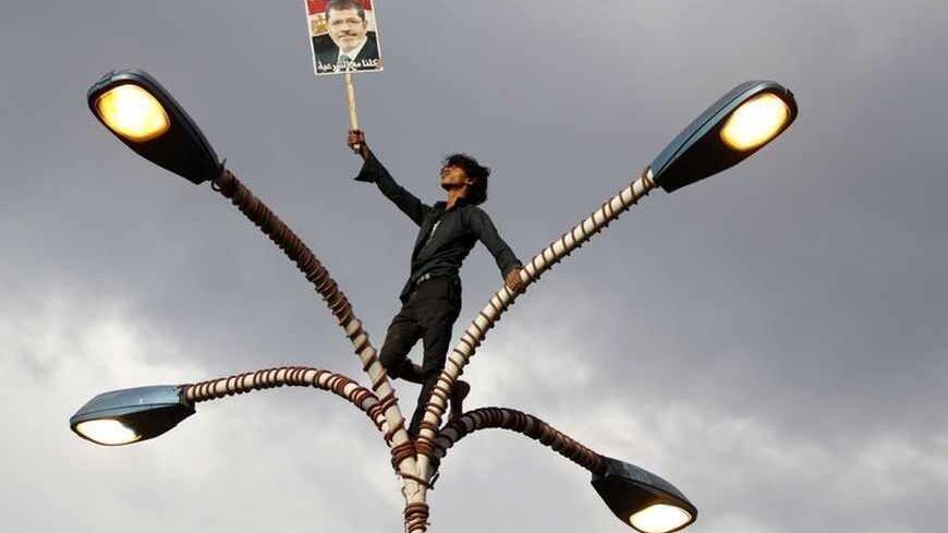 A supporter of deposed Egyptian President Mohamed Mursi holds up his photo while standing at the top of lamp posts during a march to show solidarity with his supporters in Egypt, in Sanaa August 15, 2013. The poster reads "We are all with legitimacy". REUTERS/Mohamed al-Sayaghi (YEMEN - Tags: TPX IMAGES OF THE DAY CIVIL UNREST POLITICS) - RTX12MHB