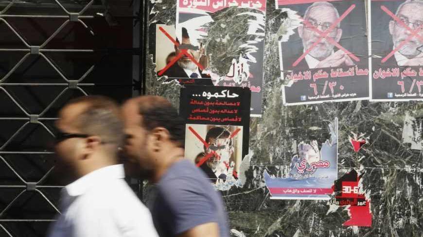 People walk in front of defected posters of ousted Egyptian President Mohamed Mursi and Muslim Brotherhood leader Mohammed Badie in downtown Cairo August 29, 2013. After a stunning reversal in which the army seized upon a tide of public discontent to overthrow freely elected President Mohamed Mursi, the powerful state apparatus appears to have all but neutralised the Muslim Brotherhood to which he belongs. Poster (R) reads, "To be on trial... No reconciliation without justice, no justice without retribution