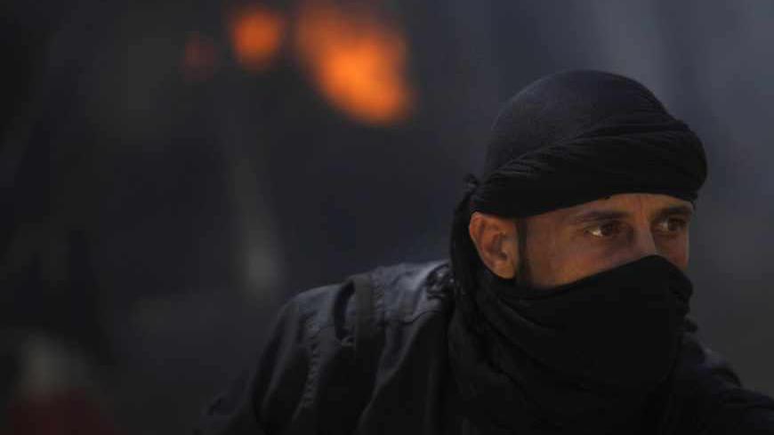 A fighter from the Islamist Syrian rebel group Jabhat al-Nusra is seen in front of a burning vehicle, caused by what activists said were missiles fired by a Syrian Air Force fighter jet from forces loyal to Syria's President Bashar al-Assad, at their base in Raqqa province, east Syria, May 12, 2013. REUTERS/Hamid Khatib (SYRIA - Tags: CONFLICT POLITICS CIVIL UNREST) - RTXZJTP