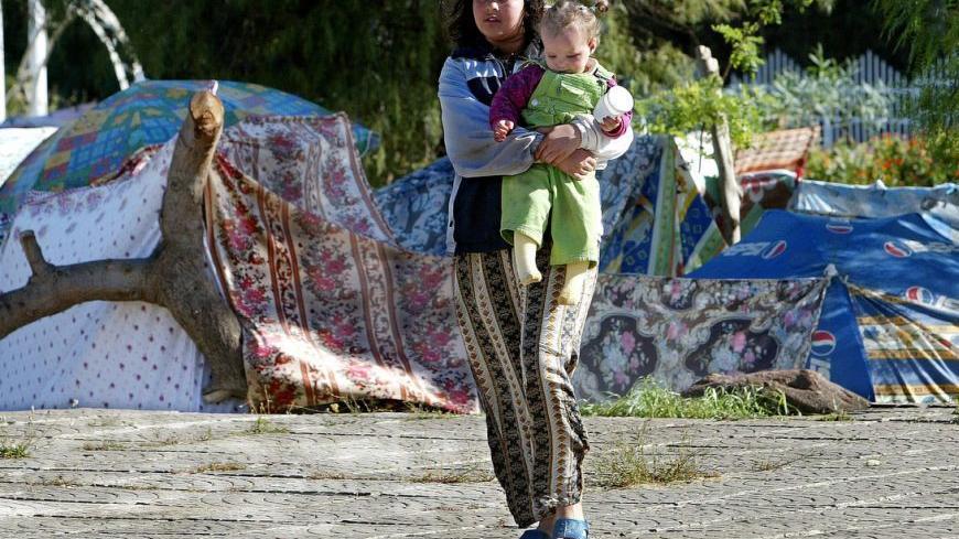 An Algerian girl holding a baby walks past makeshift shelters May 24, 2003 in the Algerian town of Boumerdes after an earthquake hit Algeria's Mediterranean coast three days ago. Hopes dwindled on Saturday of finding survivors three days after the worst earthquake in Algeria for more than two decades killed more than 1,750 people. - RTXLZF6