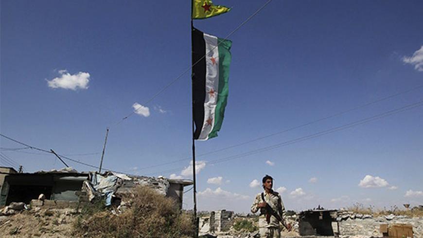 A Free Syrian Army fighter carrying his weapon, walks along a street as Syrian opposition (bottom) and Popular Protection Units (YPG) flags flutter, in Aleppo's Sheikh Maqsoud neighbourhood, June 7, 2013. Kurdish fighters from the Popular Protection Units (YPG) joined the Free Syrian Army fighters to fight against forces loyal to Syria's President Bashar al-Assad. Picture taken June 7, 2013. REUTERS/Muzaffar Salman  (SYRIA - Tags: CIVIL UNREST POLITICS CONFLICT) - RTX10USV