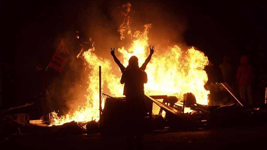 A demonstrator gestures as he stands behind burning barricades during a protest in the Tuzlucayir neighbourhood of Ankara September 9, 2013. Billed as a symbol of peace between two faiths, a new place of worship has turned Tuzlucayir, a poor suburb of Ankara, into a battleground and exposed wider sectarian tensions within Turkey. The project's blueprint envisages a Sunni mosque rising side by side with a new cemevi, or assembly house, to be used by Alevis, Turkey's biggest religious minority. But with its c