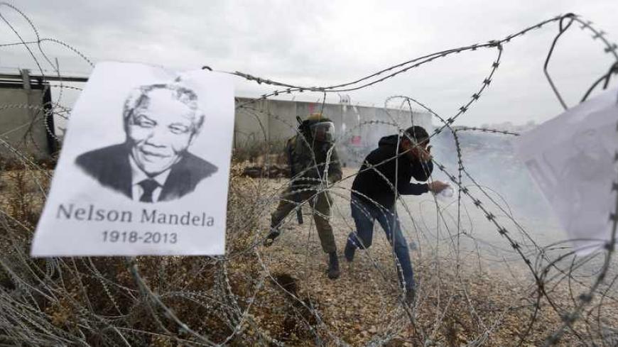 A placard depicting former South African President Nelson Mandela hangs on a barbed wire as a Palestinian protester reacts to tear gas fired by Israeli soldiers during clashes at a weekly demonstration against Jewish settlements in the West Bank village of Bilin, near Ramallah December 6, 2013. South African anti-apartheid hero Mandela died peacefully at home at the age of 95 on Thursday after months fighting a lung infection, leaving his nation and the world in mourning for a man revered as a moral giant.