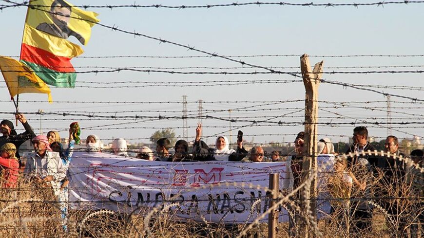 Syrian Kurds wave a flag depicting PKK's (Kurdish Workers Party) jailed leader Abdullah Ocalan as they gather on the border with Turkey, near Mardin's Nusaybin district, on October 20, 2013. Kurdish people protest against the construction by the Turkish government of a 2.5-kilometer-long wall along the border between Turkey and Syria.   AFP PHOTO/ MEHMET ENGIN        (Photo credit should read MEHMET ENGIN/AFP/Getty Images)