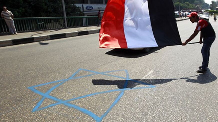 A protester waves an Egyptian flag above a Star of David symbol painted on the road during a protest in front of the Israeli embassy in Cairo August 19, 2011. Protesters gathered in front of the Israeli embassy to protest against Israel over the death of an Egyptian army officer and two security personnel who were killed during an Israeli raid on militants along the Egyptian Israeli border on Thursday. REUTERS/Amr Abdallah Dalsh (EGYPT - Tags: CIVIL UNREST POLITICS) - RTR2Q3SX