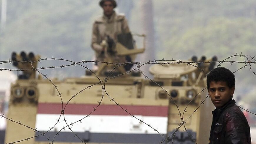 A youth stands in front of a barbed wire fence set up by soldiers after night clashes at Tahrir Square in Cairo November 20, 2013. Egyptian police fired teargas to drive protesters out of Cairo's Tahrir Square on Tuesday, breaking up a demonstration commemorating 42 protesters killed two years ago while opposing the government that took power after Hosni Mubarak's downfall. REUTERS/Amr Abdallah Dalsh  (EGYPT - Tags: POLITICS CIVIL UNREST MILITARY) - RTX15LMN
