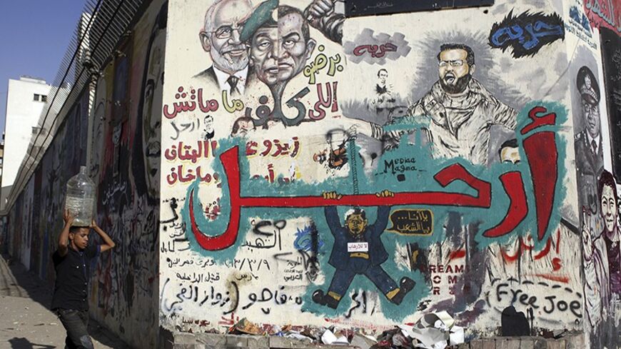 A man carrying a water container on his head walks in front of a wall filled with graffiti depicting deposed Egyptian President Mohamed Mursi with a message reading "Leave", at Tahrir Square in Cairo July 14, 2013. Egypt's interim prime minister filled senior posts on Sunday in a cabinet that will lead the country under an army-backed "road map" to restore civilian rule following overthrow of Mursi.   REUTERS/Amr Abdallah Dalsh  (EGYPT - Tags: POLITICS CIVIL UNREST) - RTX11MPT