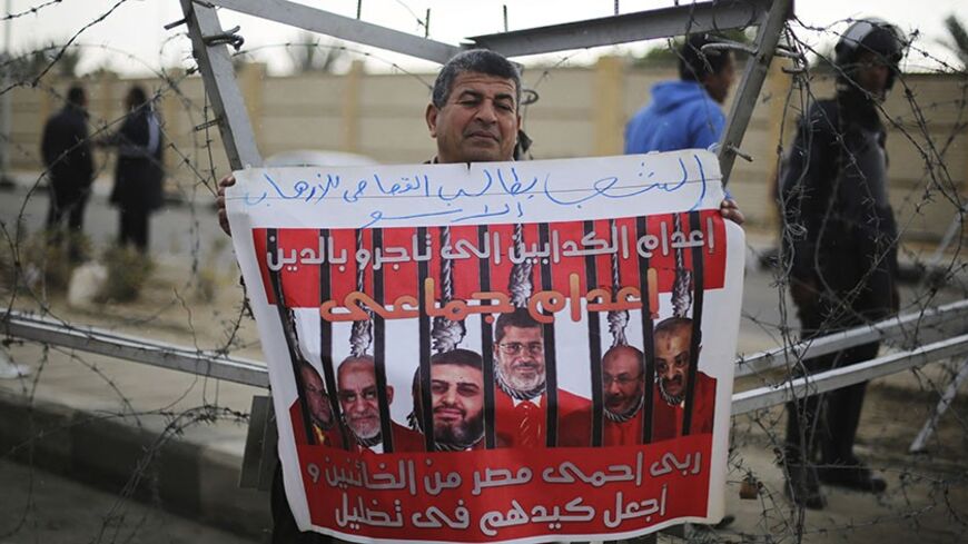 A supporter of Egypt's army chief Field Marshal Abdel Fattah al-Sisi rallies outside a police academy, where the trial of ousted Egyptian President Mohamed Mursi and members of the Muslim Brotherhood is due to take place, on the outskirts of Cairo, February 16, 2014. Mursi appeared in court on Sunday on charges of conspiring with foreign groups to commit terrorist acts in Egypt, in a further escalation of the crackdown against his Muslim Brotherhood. The poster, showing Mursi (C) and Muslim Brotherhood lead