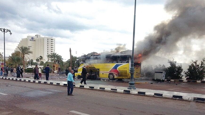 People and security officials walk and look as smoke rises from a tourist bus in the Red Sea resort town of Taba in the south Sinai, February 16, 2014. An explosion on a  tourist bus in Egypt's Sinai peninsula killed three Koreans and the Egyptian  driver on Sunday, the Interior Ministry said, an apparent turning point in an  Islamist insurgency that has gained pace since an army takeover in July. REUTERS/Stringer (EGYPT - Tags: POLITICS CIVIL UNREST TPX IMAGES OF THE DAY) - RTX18XQ7