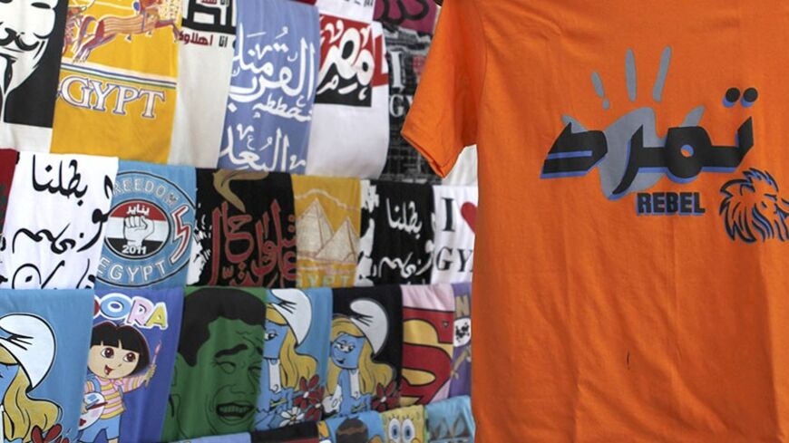 A man buys t-shirt of Tamarod, meaning opposition "Rebel" movment, while other t-shirts of Egyptian revolution are seen at Tahrir Square in Cairo June 23, 2013. The "Rebel!" alliance is campaigning to force President Mohamed Mursi to resign. Mursi's opponents say they have gathered about 15 million signatures - more than the 13 million votes that elected Mursi a year ago - on a petition calling on him to step down. REUTERS/Amr Abdallah Dalsh  (EGYPT - Tags: POLITICS CIVIL UNREST) - RTX10Y1N