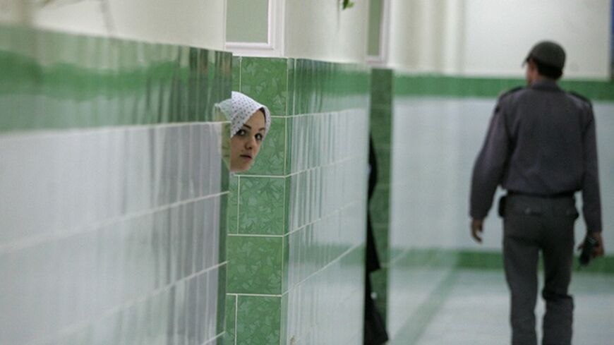 TO GO WITH AFP STORY IRAN-PRISON-RIGHTS BY STUART WILLIAMS
(FILES)An Iranian inmate peers from behind a wall as a guard walks by at the female section of the infamous Evin jail, 13 June 2006. From the road it is easy to miss. A small outhouse and a sign saying "Evin House of Detention" give no hint of the huge complex of guard towers and cells that lies behind.     AFP PHOTO/ATTA KENARE (Photo credit should read ATTA KENARE/AFP/Getty Images)