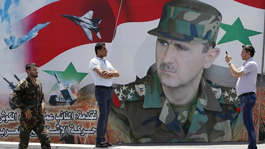 A man takes a photo of his friend in front of a poster of Syria's President Bashar al-Assad at Umayyad Square in Damascus May 16, 2014. Syria is holding a presidential election for June 3, preparing the ground for Assad to defy widespread opposition and extend his grip on power, days after he said the civil war was turning in his favour. Opponents have dismissed the vote as a farce.   REUTERS/Khaled al-Hariri (SYRIA - Tags: POLITICS ELECTIONS CIVIL UNREST CONFLICT) - RTR3PGCV