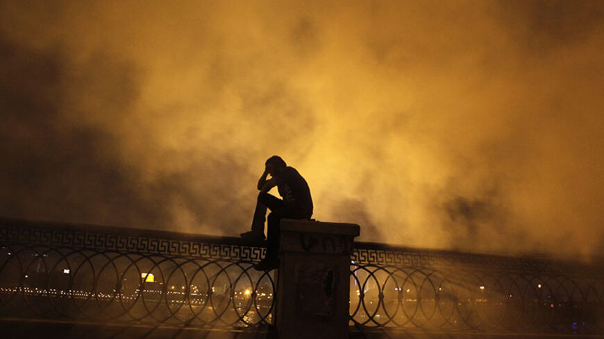 A protester covers his face as he stands in front of tear gas during clashes with riot police along a road at Kornish El Nile which leads to the U.S. embassy, near Tahrir Square in Cairo September 15, 2012. Clashes near the U.S. Embassy in central Cairo between police and Egyptians incensed over a film denigrating the Prophet Mohammad entered their fourth day early on Saturday, leaving one protester dead and dozens more injured.  REUTERS/Amr Abdallah Dalsh  (EGYPT - Tags: POLITICS CIVIL UNREST RELIGION) - R