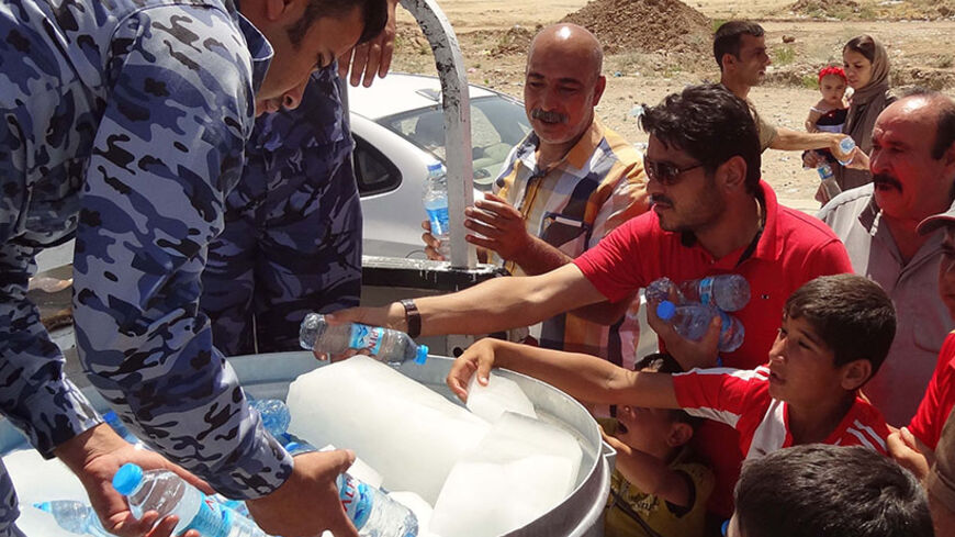 Iraqi military personnel distribute water to Shiite Iraqi Kurds, known as "Shabak", displaced by fierce fighting between Kurdish peshmerga forces and jihadist militants from the Islamic State (IS) after arriving on the road between Kirkuk and Arbil having fled the area of Bartala near the northern Iraqi city of Mosul, on August 8, 2014. Jihadists seized Iraq's largest dam north of their hub of Mosul, giving them control over the supply of water and electricity for a vast area, officials said. AFP PHOTO / MA