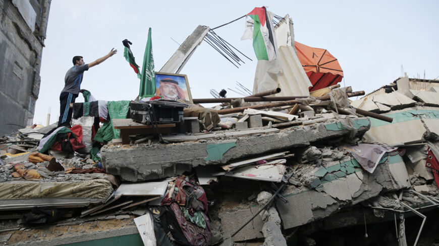 A Palestinian man throws a flag atop the rubble of the home of Hamas Gaza leader Ismail Haniyeh, which Gaza's interior ministry said was hit by a missile fired by Israeli aircraft before dawn on Tuesday, causing damage but no casualties, in Gaza City July 29, 2014. Israel's military pounded targets in the Gaza Strip on Tuesday after Prime Minister Benjamin Netanyahu said his country needed to be prepared for a long conflict in the Palestinian enclave, squashing any hopes of a swift end to 22 days of fightin