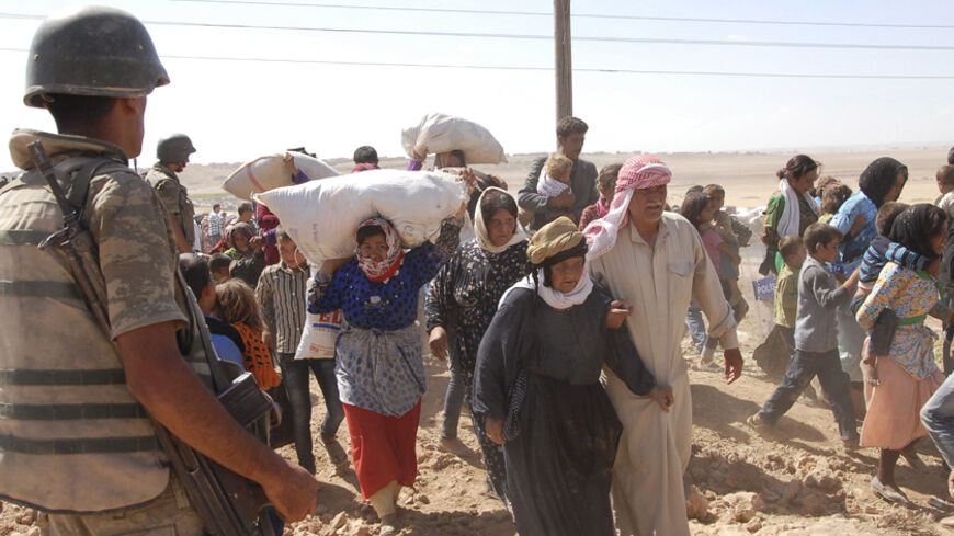 A Turkish soldier stands guard as Syrian Kurds cross the border fence into Turkey near the southeastern town of Suruc in Sanliurfa province, September 19, 2014. Several thousand Syrian Kurds began crossing into Turkey on Friday fleeing Islamic State fighters who advanced into their villages, prompting warnings of massacres from Kurdish leaders. Islamic State (IS) fighters have seized villages in northern Syria over the past two days and are besieging the mainly Kurdish town of Ayn al-Arab, known as Kobani i