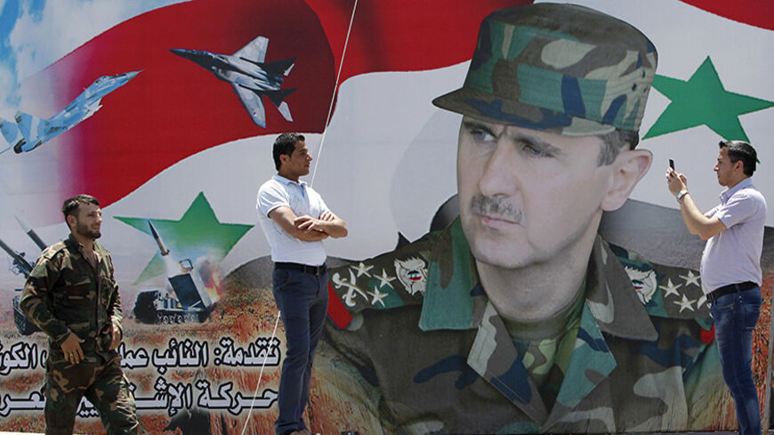 A man takes a photo of his friend in front of a poster of Syria's President Bashar al-Assad at Umayyad Square in Damascus May 16, 2014. Syria is holding a presidential election for June 3, preparing the ground for Assad to defy widespread opposition and extend his grip on power, days after he said the civil war was turning in his favour. Opponents have dismissed the vote as a farce.   REUTERS/Khaled al-Hariri (SYRIA - Tags: POLITICS ELECTIONS CIVIL UNREST CONFLICT) - RTR3PGCV