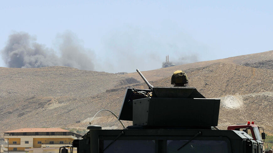 A Lebanese army soldier sits atop an army vehicle at the entrance of the Sunni Muslim border town of Arsal, in eastern Bekaa Valley, as smoke rises during clashes between Lebanese army soldiers and Islamist militants August 4, 2014. The Lebanese army advanced into a border town that was attacked by Islamists in an incursion from Syria at the weekend, finding the bodies of 50 militants, a Lebanese security official said.     REUTERS/Hassan Abdallah    (LEBANON - Tags: POLITICS CIVIL UNREST MILITARY TPX IMAGE