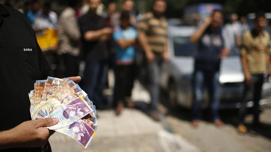 A Palestinian employee paid by the Palestinian Authority shows money to the camera after withdrawing cash from an ATM machine outside a bank, in Gaza City June 11, 2014. Gaza's public sector union suspended protests on Wednesday that had paralysed the local economy and threatened the deal on a Palestinian unity government but said it would resume its action if its members were not promptly paid. The pay dispute involving some 40,000 public servants erupted last week shortly after Hamas, which has ruled Gaza