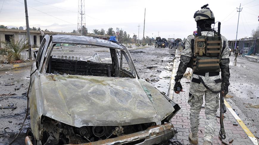A member of the Iraqi security forces walks past a destroyed vehicle belonging to Islamic State militants during an intensive security deployment on the outskirts of Samarra December 14, 2014. Picture taken December 14, 2014. REUTERS/Stringer (IRAQ - Tags: CIVIL UNREST POLITICS MILITARY) - RTR4I0GG