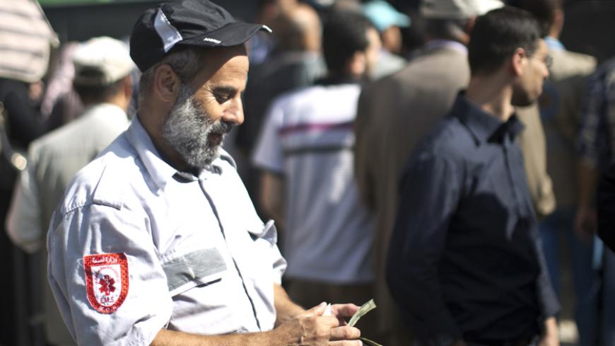 A Palestinian employee of the former Hamas government counts his money outside a post office in Gaza City on October 29, 2014 after receiving 1,200 US dollars which is part of his wages that has been delayed for months. The Palestinian national unity government headed by prime minister Rami Hamdallah sent the previous day roughly 30 million dollars by car across the Erez border crossing from the West Bank to the Gaza Strip to pay 24,000 former employees. AFP PHOTO / MAHMUD HAMS        (Photo credit should r