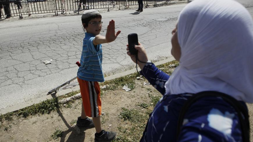 A Jewish boy lifts his hand to prevent a Palestinian from taking his picture near a police barrier cordoning off a building the day after Israeli police evicted Jewish settlers who occupied it in the West Bank city of Hebron April 5, 2012. Israeli police evicted Jewish settlers on Wednesday from the building they said they had bought from a Palestinian in the heart of Hebron, a frequent flashpoint in the Israeli-Palestinian conflict. REUTERS/Ammar Awad (WEST BANK - Tags: POLITICS MILITARY CIVIL UNREST) - RT