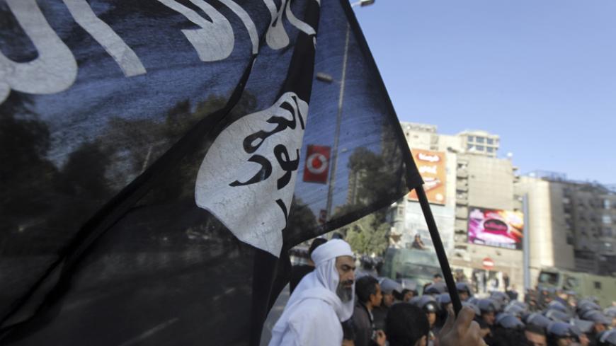 An Islamist protester holds a Salafist flag with Arabic words that read "There is no God but Allah and Mohammad is his prophet" as Egyptian security forces stand guard during a protest against the French operation in Mali outside the French embassy in Cairo January 18, 2013. REUTERS/Amr Abdallah Dalsh  (EGYPT - Tags: POLITICS CIVIL UNREST) - RTR3CLWR