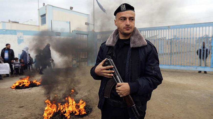 A Palestinian policeman loyal to Hamas stands guard near burning tyres during a protest by Palestinians calling for reconstruction of their houses that witnesses said were destroyed by Israeli shelling during a 50-day war last summer, outside a United Nations food distribution center in Rafah in the southern Gaza Strip February 16, 2015. REUTERS/Ibraheem Abu Mustafa (GAZA - Tags: POLITICS CIVIL UNREST CRIME LAW) - RTR4PQSX