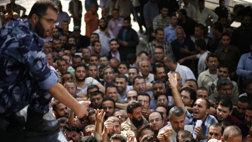 A Palestinian policeman gestures as Hamas-hired civil servants wait to receive a payment in Gaza City October 29, 2014. Some 24,000 civil servants hired by the Islamist group Hamas, many of whom have not received a full salary in almost a year, finally got some pay on Wednesday from the new Palestinian unity government based in the West Bank. The funds were supplied by the gas-rich kingdom of Qatar, which is an ally of Hamas. But the fact the cash was delivered by the West Bank administration gave a boost t