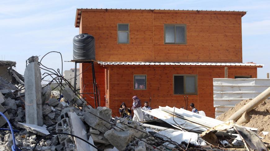 Palestinians, whose house was destroyed by what witnesses said was Israeli shelling during a 50-day war last summer, sit outside their wooden shelter donated by Catholic Relief Services, east of Khan Younis in the southern Gaza Strip February 16, 2015. Aid agencies struggling to shelter thousands of Gazans made homeless by war have resorted to building makeshift temporary homes out of metal and wood to evade Israeli restrictions on imports into the territory. Around 150,000 families are still homeless after