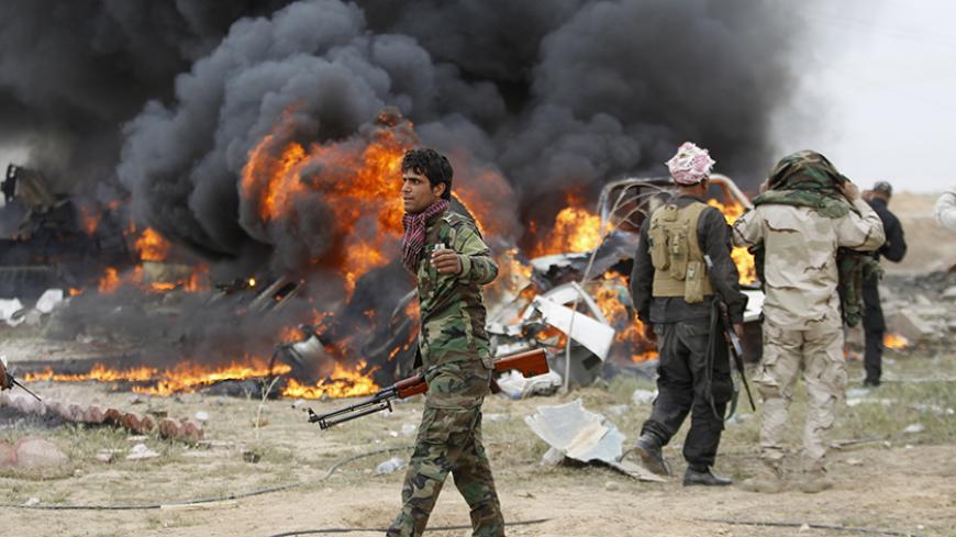 Shi'ite fighters known as Hashid Shaabi walk as smoke rises from an explosives-laden military vehicle driven by an Islamic State suicide bomber which exploded during an attack on the southern edge of Tikrit March 12, 2015. Iraqi security forces and mainly Shi'ite militia exchanged fire sporadically with Islamic State fighters in Tikrit on Thursday, a day after they pushed into Saddam Hussein's home city in their biggest offensive yet against the militants. A Reuters photographer saw one car bomb explode on 