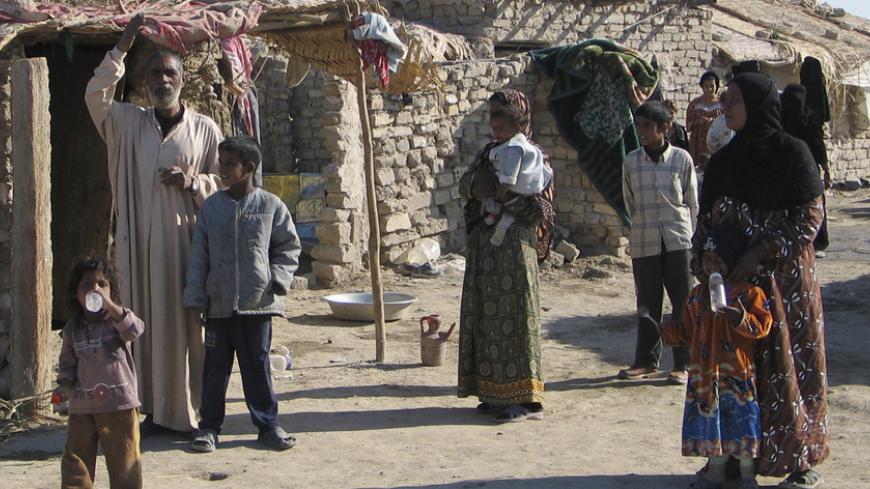 Iraqi gypsy families gather outside their shack that serves as their home in the southern Iraqi city of Diwaniya January 4, 2006. Scorned by religious Muslims and barely tolerated by the rest of society, Iraq's Gypsies have a precarious existence. Lacking education or skills, they form one of the lower rungs of Iraq's social system. To match feature IRAQ GYPSIES REUTERS/Imad Al-Khozai - RTR17RDG