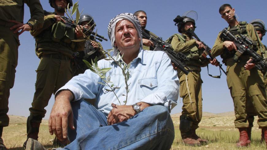 Israeli soldiers stand guard as a Palestinian farmer sits on the ground after planting olive trees during a protest against what Palestinians say is land confiscation for Jewish settlements in the Jordan Valley, a hotly contested part of the occupied West Bank April 8, 2014. REUTERS/Abed Omar Qusini (WEST BANK - Tags: POLITICS AGRICULTURE MILITARY) - RTR3KEMR