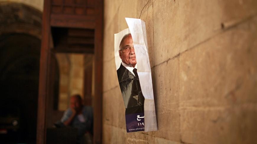 A man sits outside a shop as a poster of presidential candidate Ahmed Shafiq is seen hanging on a wall in Cairo June 13, 2012. The Brotherhood's Mohamed Mursi will face Shafiq, the last prime minister of ousted leader Hosni Mubarak, in a presidential run-off on June 16 and 17, the climax of Egypt's first free leadership contest after 16 months of military rule. REUTERS/Suhaib Salem (EGYPT - Tags: POLITICS CIVIL UNREST) - RTR33JB4