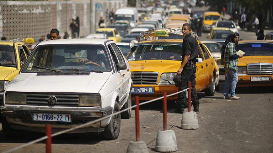 A Palestinian policeman loyal to Hamas stands next to lines of cars as drivers wait to fill them with fuel outside a petrol station in Gaza City September 15, 2013. The Gaza Strip is experiencing a shortage in fuel smuggled in via tunnels dug beneath the Gaza-Egypt border as Egyptian security forces have stepped up a crackdown campaign on the tunnels since July, residents said. REUTERS/Mohammed Salem (GAZA - Tags: POLITICS TRANSPORT) - RTX13LZS