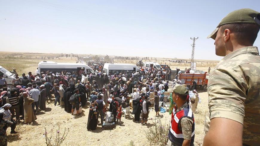 Turkish soldiers stand guard as Syrian refugees wait for transportation after crossing into Turkey from the Syrian town of Tal Abyad, near Akcakale in Sanliurfa province, Turkey, June 10, 2015. Thousands of people crossed from Syria into Turkey on Wednesday to flee a battle pitting Islamist insurgents against Kurdish and opposition forces for the Syrian border town of Tel Abyad. REUTERS/Osman Orsal - RTX1FYCO