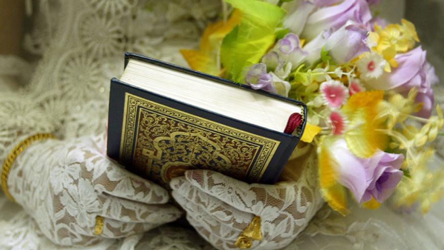 Iraqi newlywed Naheb Saidi, 25, sits holding a Koran Holy book and a bouquet of flowers during her wedding party in Baghdad July 1, 2004. [As the world watched Saddam Hussein's first court appearance, the couple took their vows to lead a new life together.] - RTXMPMI