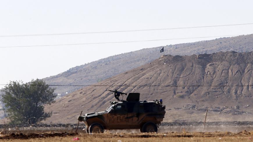 A black flag belonging to Islamic State is seen near the Syrian town of Kobani as a Turkish army vehicle takes up position on the Turkish-Syrian border near the southeastern town of Suruc in Sanliurfa province October 7, 2014. Islamic State fighters advanced into the south west of the Syrian Kurdish town of Kobani overnight, a monitoring group said on Tuesday, taking several buildings to gain attacking positions from two sides of the city. REUTERS/Umit Bektas (TURKEY - Tags: CIVIL UNREST MILITARY CONFLICT