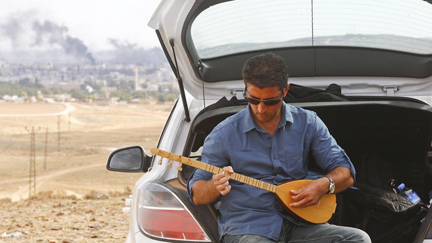 A Turkish Kurd plays the citar as smoke rises from the Syrian town of Kobani, as seen from the Mursitpinar crossing on the Turkish-Syrian border in Sanliurfa province October 26, 2014.  REUTERS/Kai Pfaffenbach (TURKEY - Tags: MILITARY CONFLICT POLITICS SOCIETY) - RTR4BMFX