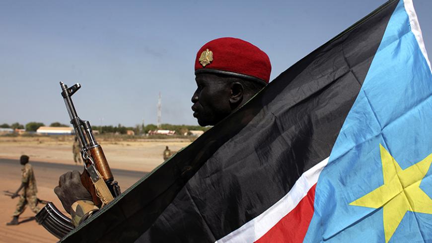 An SPLA soldier is pictured behind a South Sudan flag as he sits on the back of a pick-up truck in Bentiu, Unity state January 12, 2014. South Sudan's army said on Friday it had regained the rebel-held town of Bentiu, restoring government control of Unity state where oil production had been halted by fighting. The rebels said they made a "tactical withdrawal" from Bentiu to avoid civilian casualties. REUTERS/Andreea Campeanu (SOUTH SUDAN - Tags: CIVIL UNREST POLITICS CONFLICT) - RTX17AO2