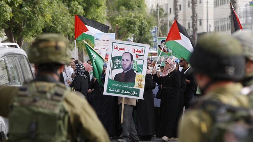 Israeli soldiers stand guard as Palestinians hold national flags and posters of jailed relatives during a protest in solidarity with prisoners on hunger strike,in the West Bank city of Hebron June 4, 2014. Some 120 Palestinians jailed without trial in Israel have been on an open-ended hunger strike, eating only salt and drinking water, since April 24 to demand an end to so-called "administrative detention". REUTERS/Mussa Qawasma (WEST BANK - Tags: POLITICS CIVIL UNREST) - RTR3S7JN