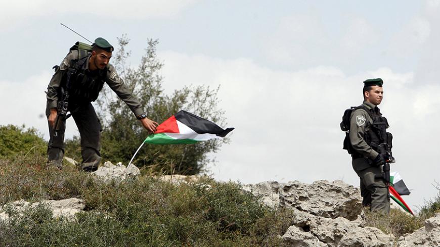 Israeli border policeman remove Palestinian flags during a demonstration by Palestinians marking Land Day and against Jewish settlements in Wadi Foukeen near the West Bank city of Bethlehem March 30, 2015. Palestinians mark Land Day on March 30, the annual commemoration of protests in 1976 against Israel's appropriation of Arab-owned land in the Galilee. REUTERS/Mussa Qawasma - RTR4VGRL