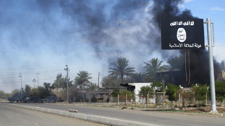 Smoke raises behind an Islamic State flag after Iraqi security forces and Shiite fighters took control of Saadiya in Diyala province from Islamist State militants, November 24, 2014. Iraqi forces said on Sunday they retook two towns north of Baghdad from Islamic State fighters, driving them from strongholds they had held for months and clearing a main road from the capital to Iran. There was no independent confirmation that the army, Shi'ite militia and Kurdish peshmerga forces had completely retaken Jalawl
