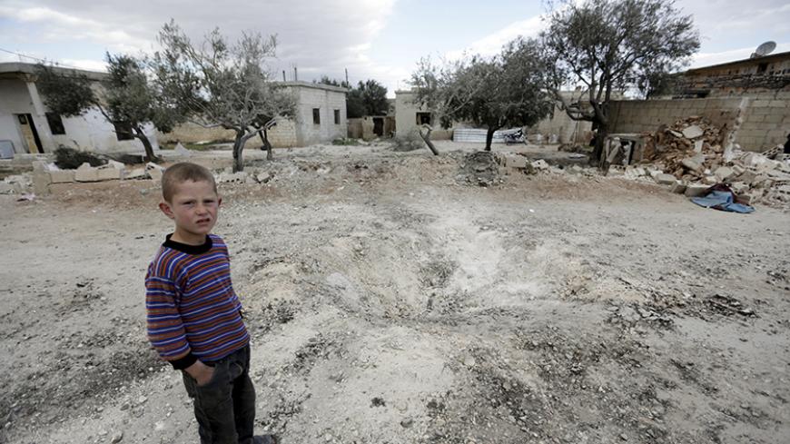 A boy stands near a hole in the ground after a shell fell in the rebel-held town of Jarjanaz, southern Idlib countryside, Syria March 5, 2016. REUTERS/Khalil Ashawi         TPX IMAGES OF THE DAY      - RTS9EO7