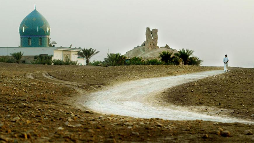 BORSIPPA, IRAQ - JUNE 8:  A man walks down a road in the shadow of a Mesopotamian ziggurat (C) and a shrine to the prophet Abraham (L) June 8, 2003 in Borsippa, Iraq. The ziggurat, a temple tower, was built by King Nebuchadnezzar about 2,500 years ago. Iraq's cultural heritage has been threatened by the looting of museums and archeological sites following the war.  (Photo by Mario Tama/Getty Images)  