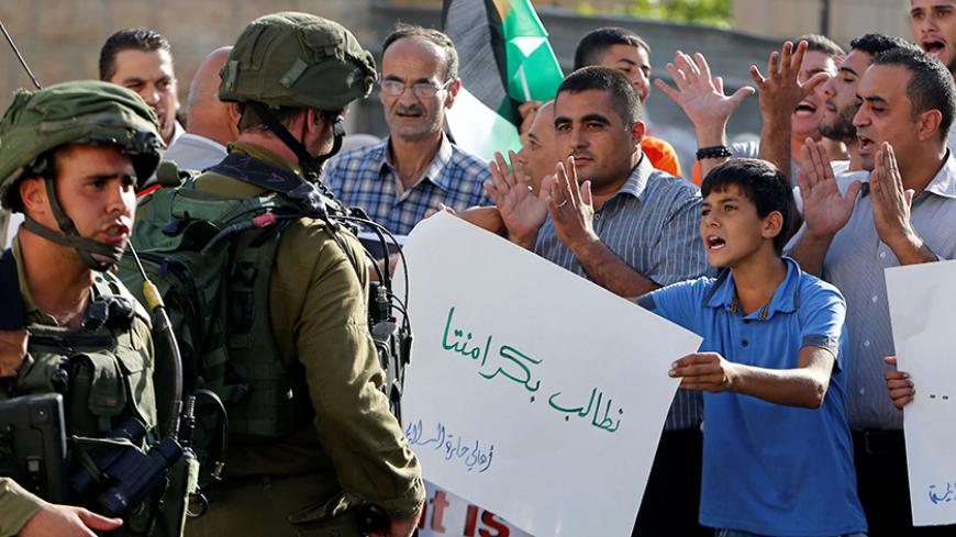 A Palestinian boy holds a sign that reads "we demand our dignity" in front of Israeli soldiers during a protest calling for the reopening of a closed street in the West Bank city of Hebron August 24, 2016. REUTERS/Mussa Qawasma - RTX2MW1E