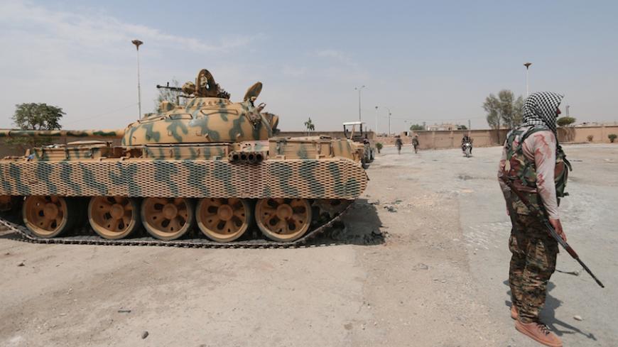 A Kurdish fighter from the People's Protection Units (YPG) carries his weapon as he stands past a tank in the Ghwairan neighborhood of Hasaka, Syria, August 22, 2016. REUTERS/Rodi Said - RTX2MKNR
