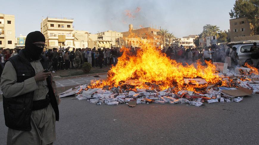 A fighter from Islamic State in Iraq and the Levant (ISIL) stands near burning confiscated cigarettes in the city of Raqqa April 2, 2014. REUTERS/Stringer (SYRIA - Tags: POLITICS CIVIL UNREST CONFLICT RELIGION SOCIETY) - RTR3JOPD